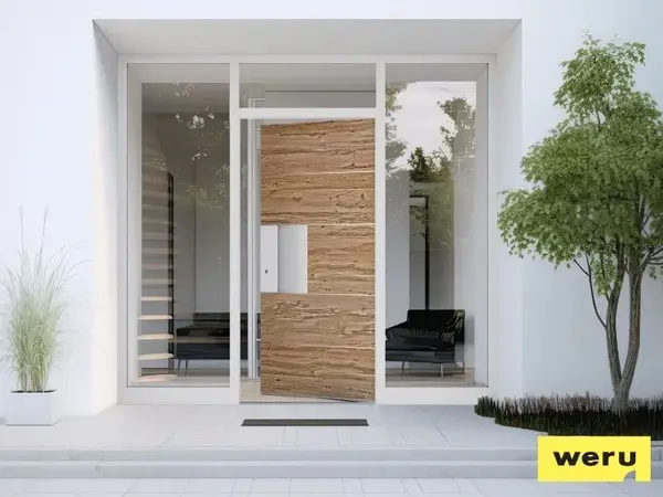 Moderne Haustür aus Holz und Glas mit Seitenteilen, umgeben von Pflanzen und Sitzbereich.