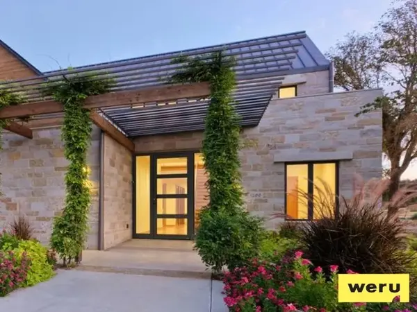 Modernes Einfamilienhaus mit Natursteinfassade, großen Fenstern und begrüntem Eingang.
