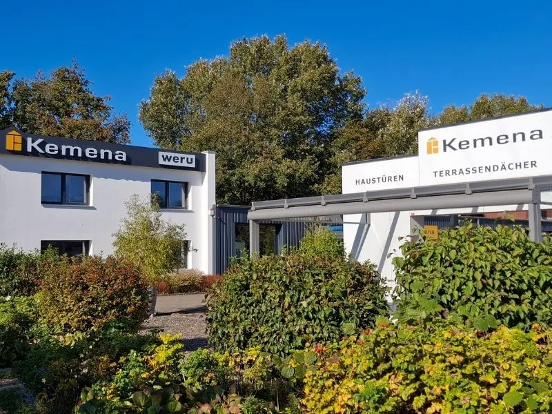 Firmengebäude von Kemena mit Werbung für Haustüren und Terrassendächer im Grünen.